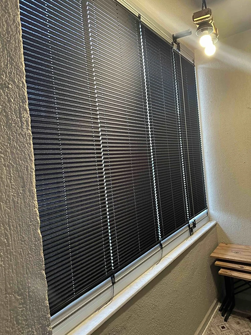 Balkon boyunca takılı antrasit plise perdeler